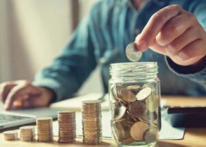 A man putting a coin into a glass jar, indicating he is saving or investing.