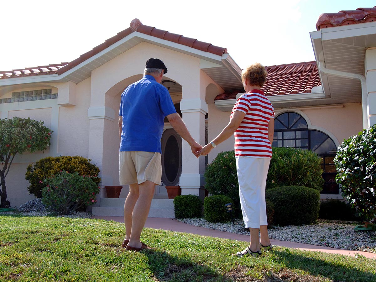 Senior couple holding hands in front of a house