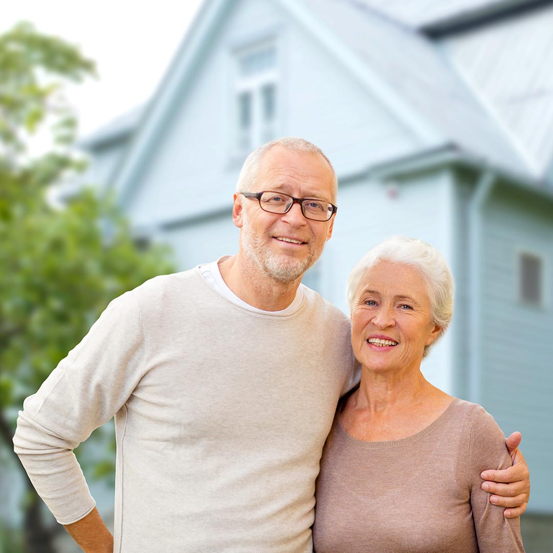 smiling senior couple standing in front of a house