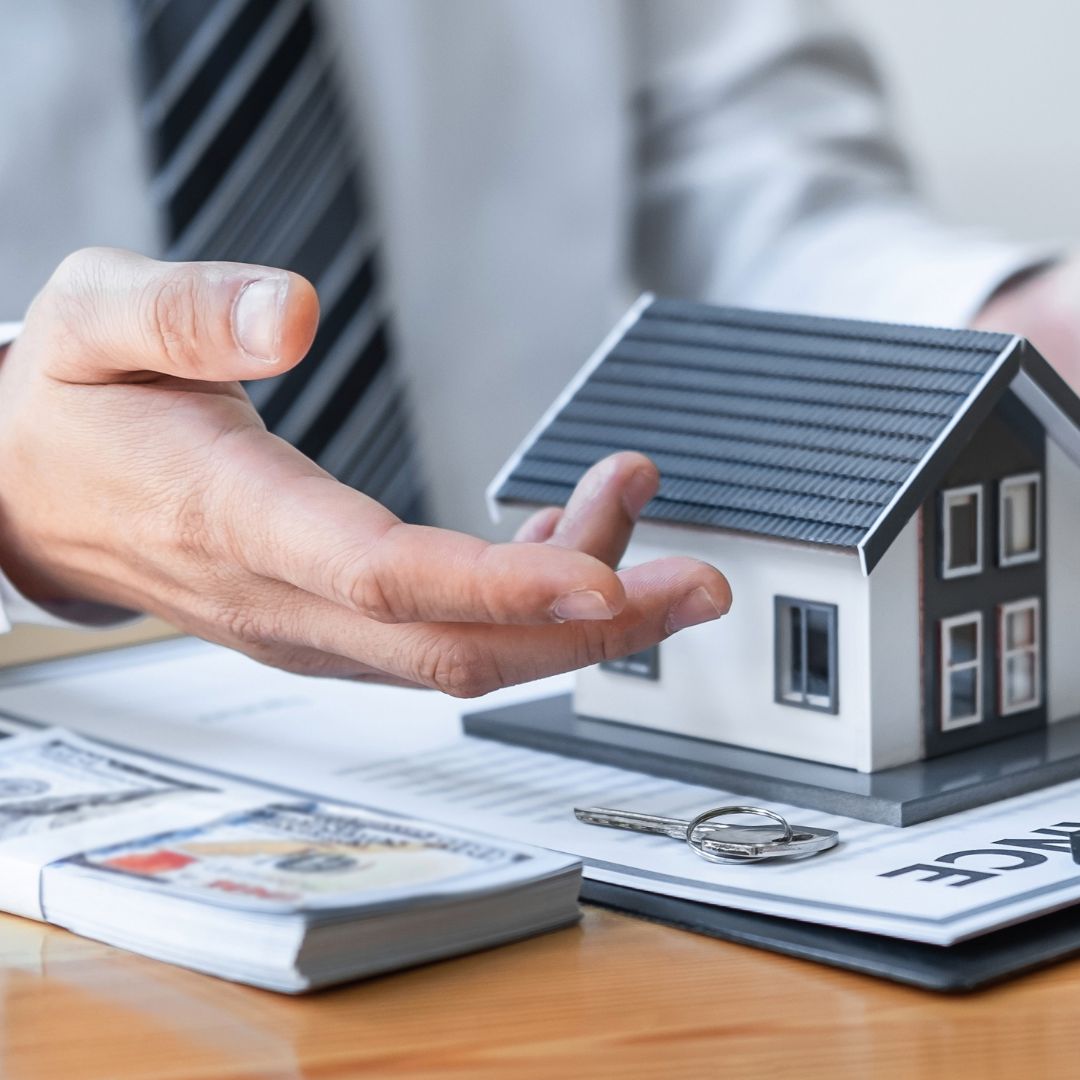 a person with a model house, a stack of money, and paperwork