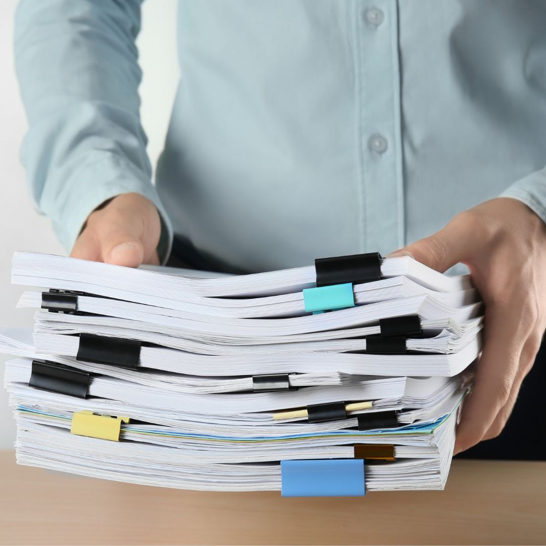 a person holding several large stacks of paperwork
