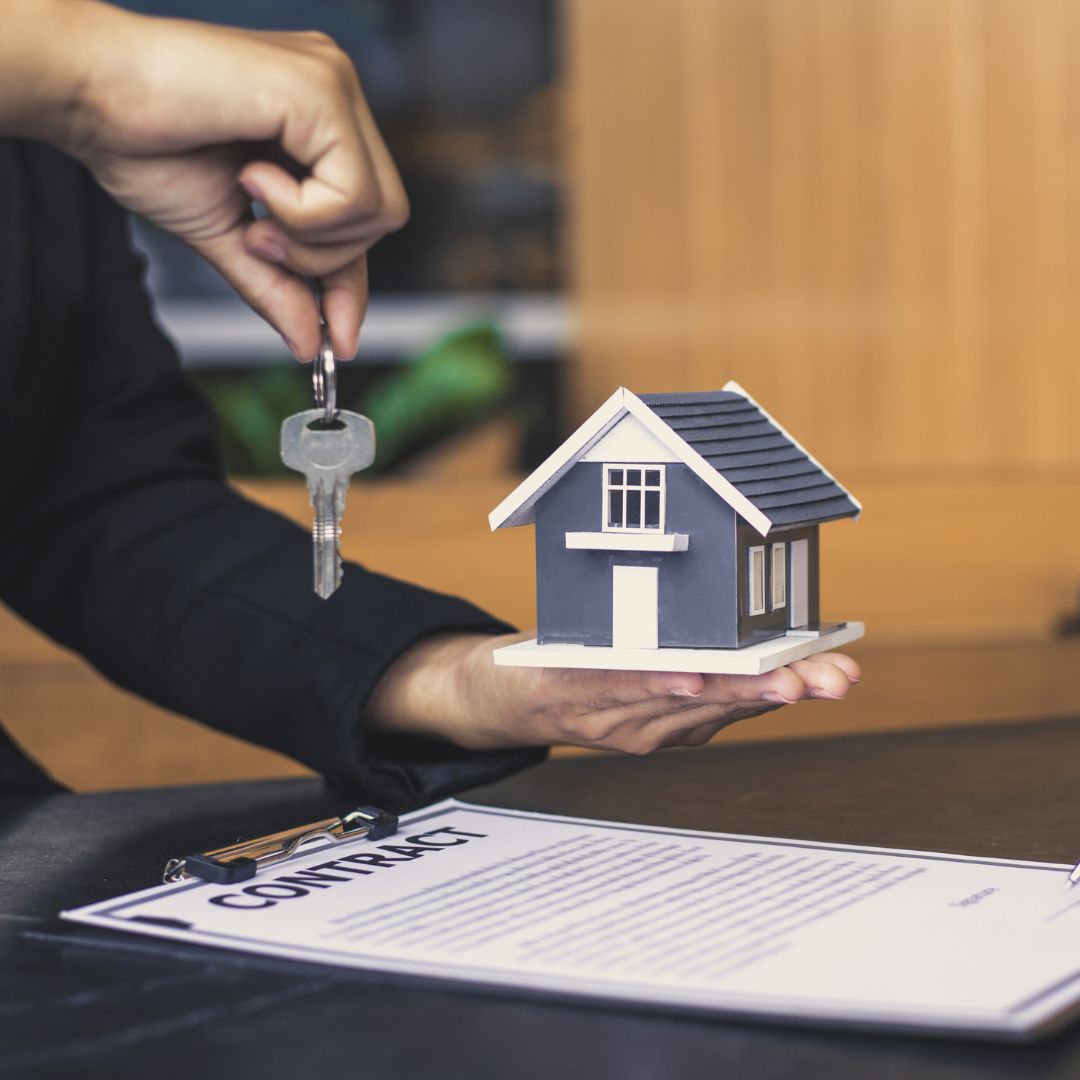 a person holding a small model home and a key