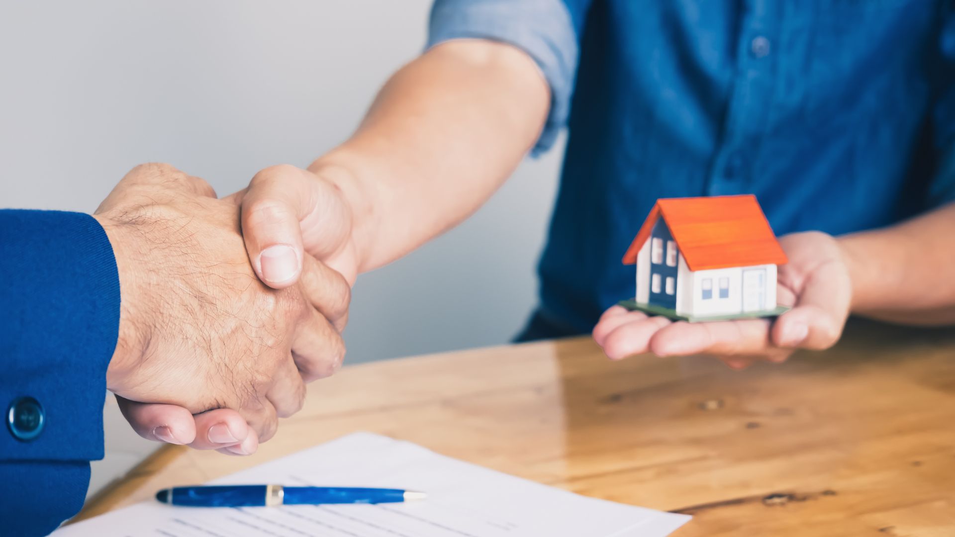 People shaking hands next to a miniature model of a house