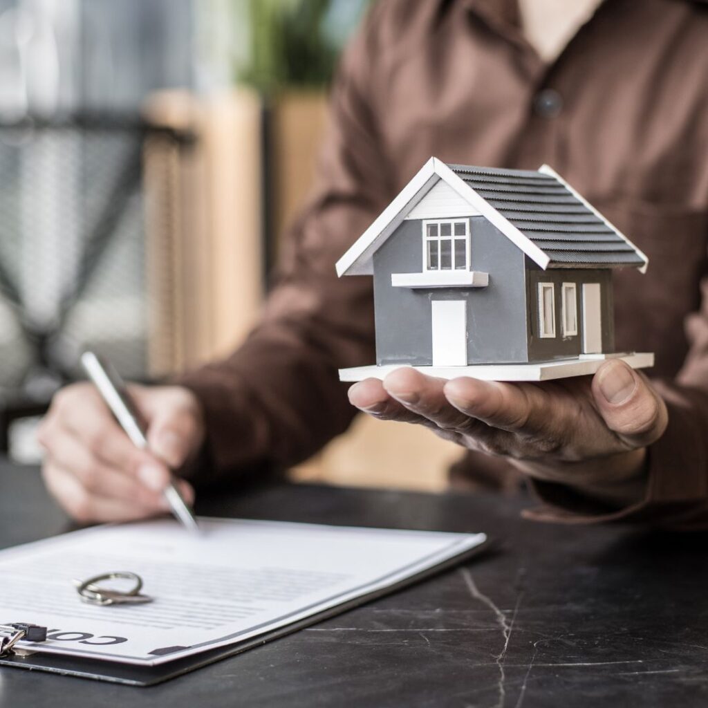 A person signing a contract and holding a miniature model of a house