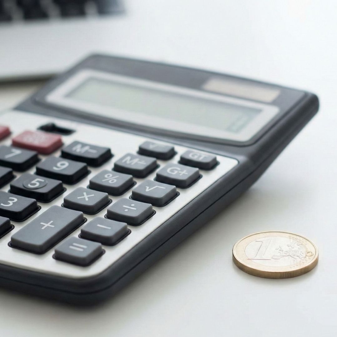 A close-up of a calculator and a single coin on a desk.