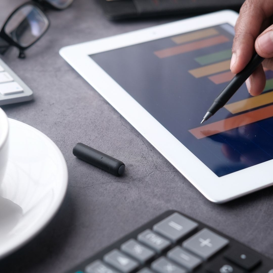 A close-up view of a hand using a stylus on a tablet showing a data chart, with a coffee cup nearby.